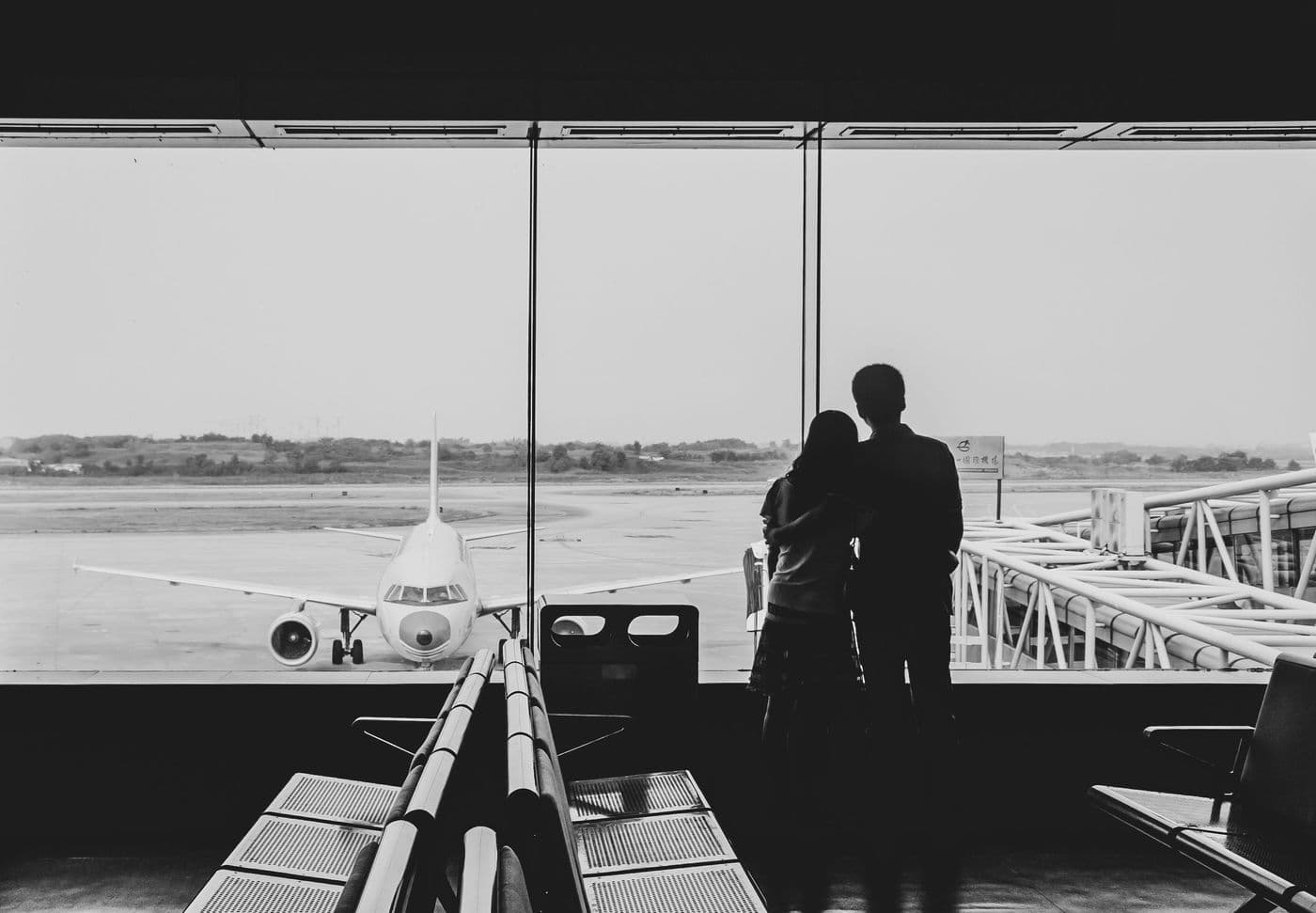 A couple watching a plane on the tarmac through an airport window